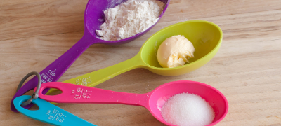 Purple plastic spoon with flour, Lime-green plastic spoon with butter and pink plastic spoon with sugar.
