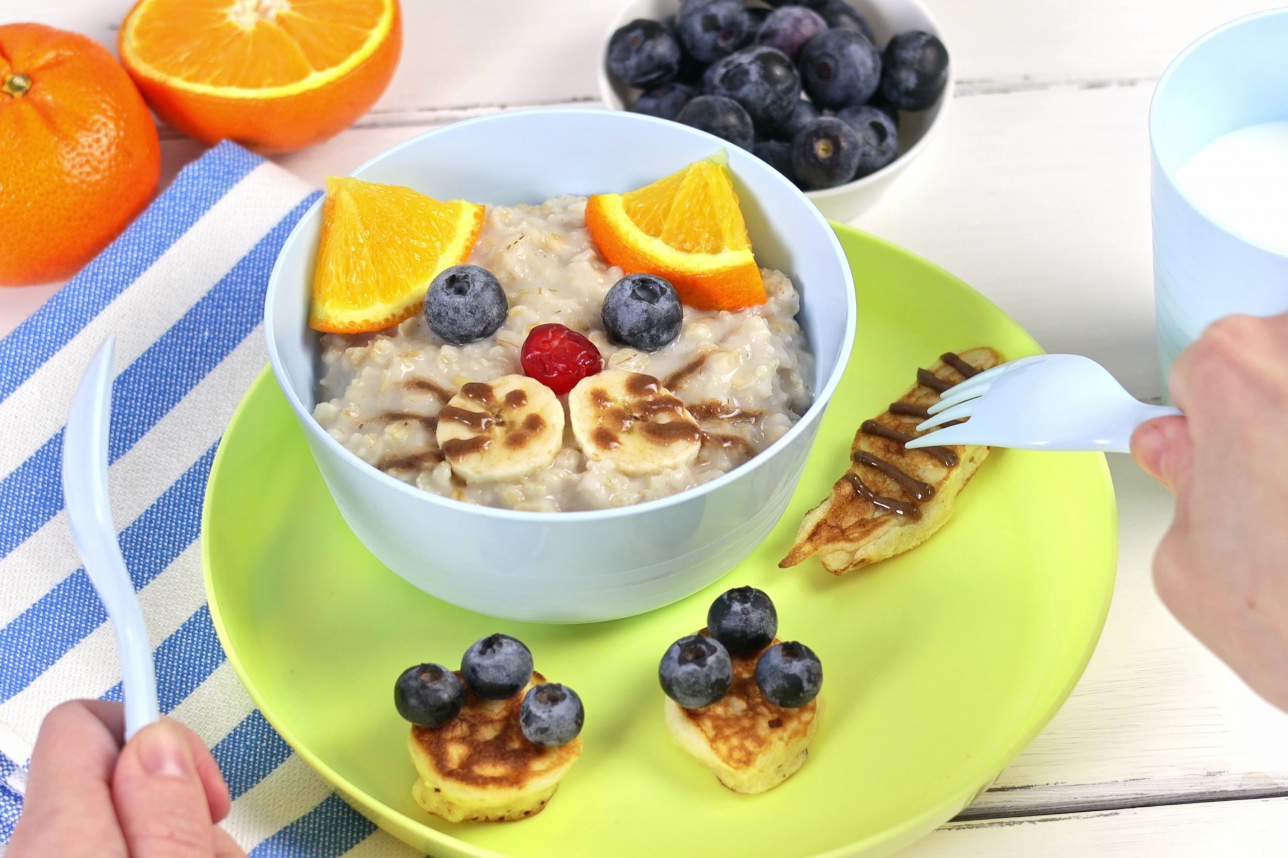 Funny bowls of oatmeal with cat faces, fruits and berries, food idea for kids, top view